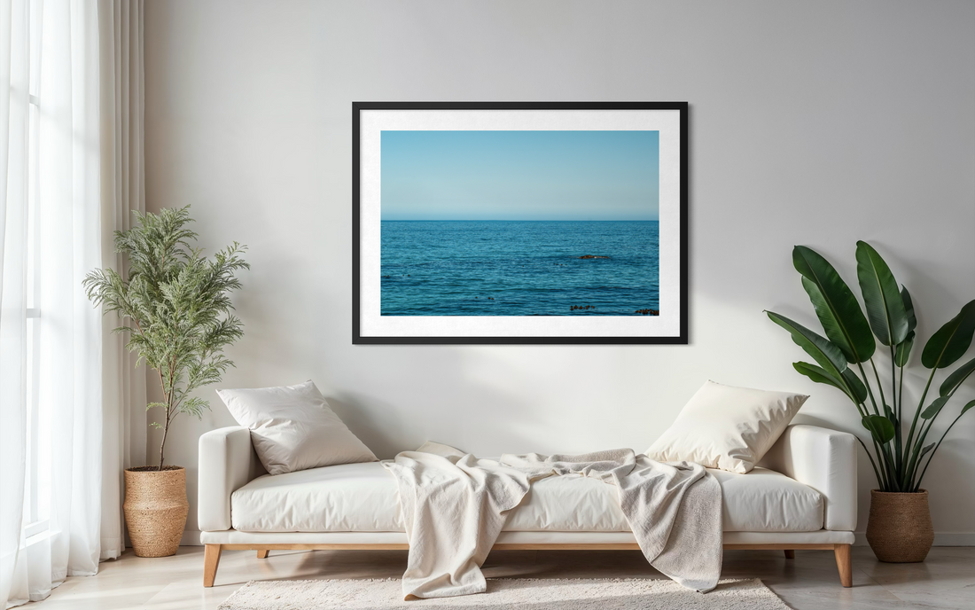 Large-format coastal fine art print displayed in a minimal Scandinavian living room with natural linen sofa and warm afternoon light